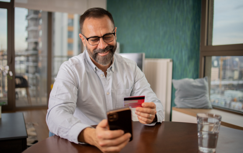 Smiling man making an online purchase with a credit card and smartphone, showcasing seamless eCommerce branding.